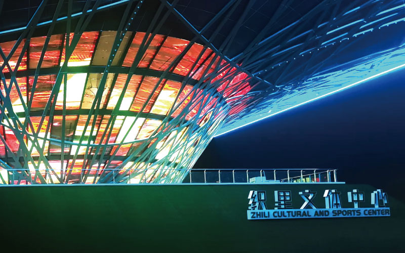 位于浙江湖州的织里体裁中间，是一座大型异形钢架布局优游。三思为其定制近1000平米通明屏，利用高清LED通明屏及节制体系，将其打造成了一幅巨型优游媒体立面。